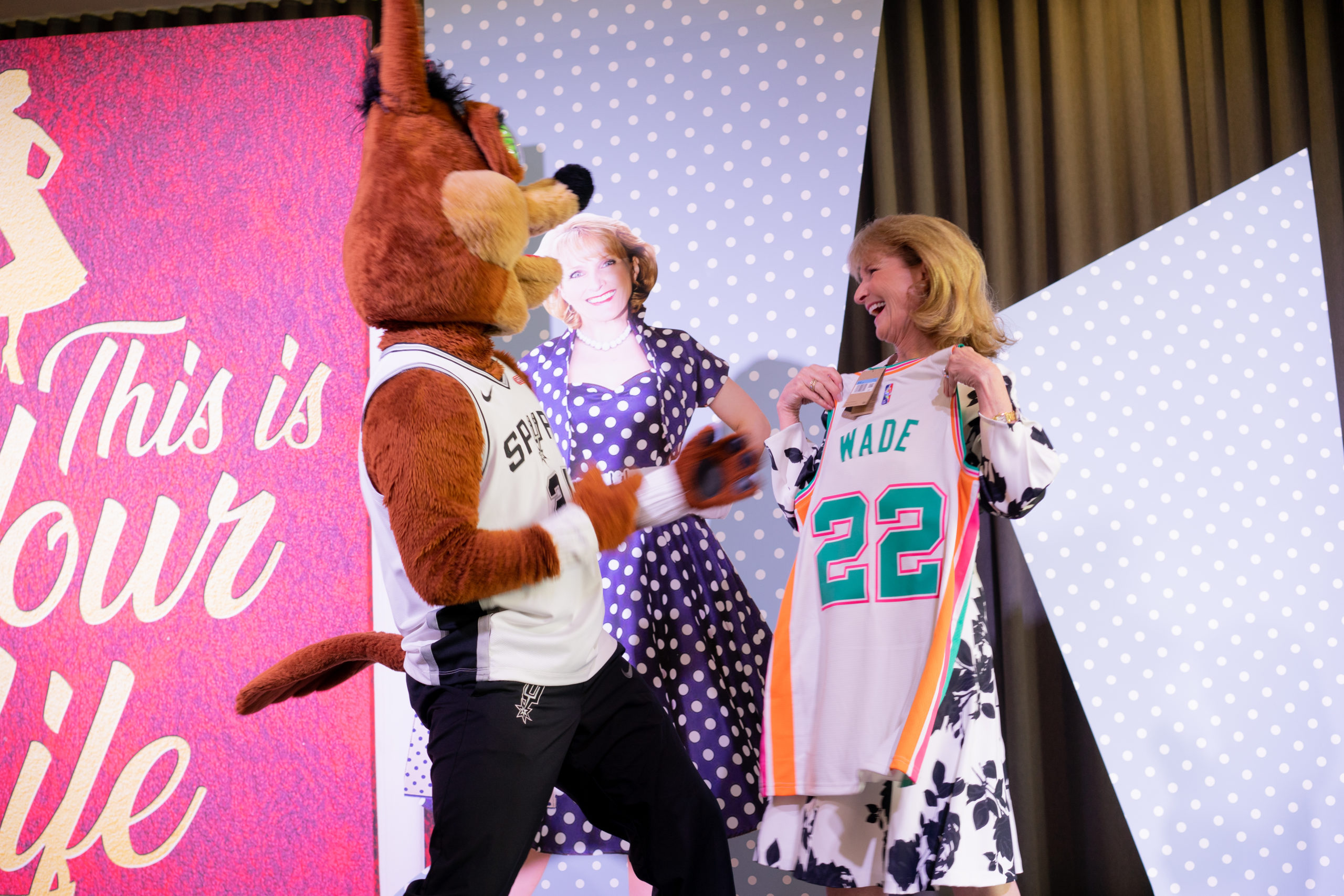 Suzanne Wade smiles at the Spurs Coyote while holding her new custom Spurs jersey