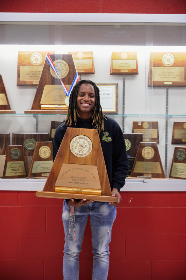 Kiara holds a state champion award in front of a trophy case
