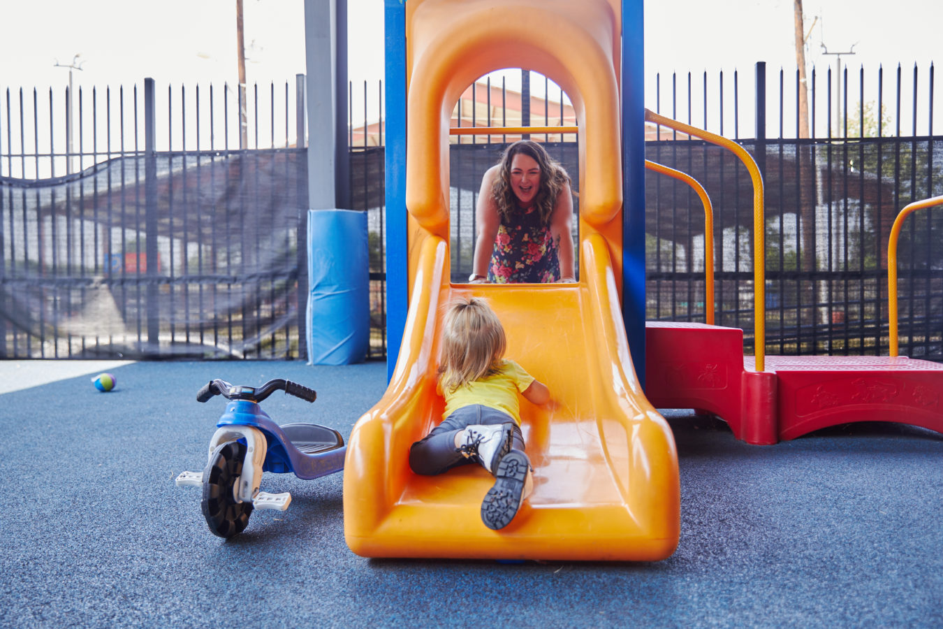 A child lays on a slide while looking up at an adult woman