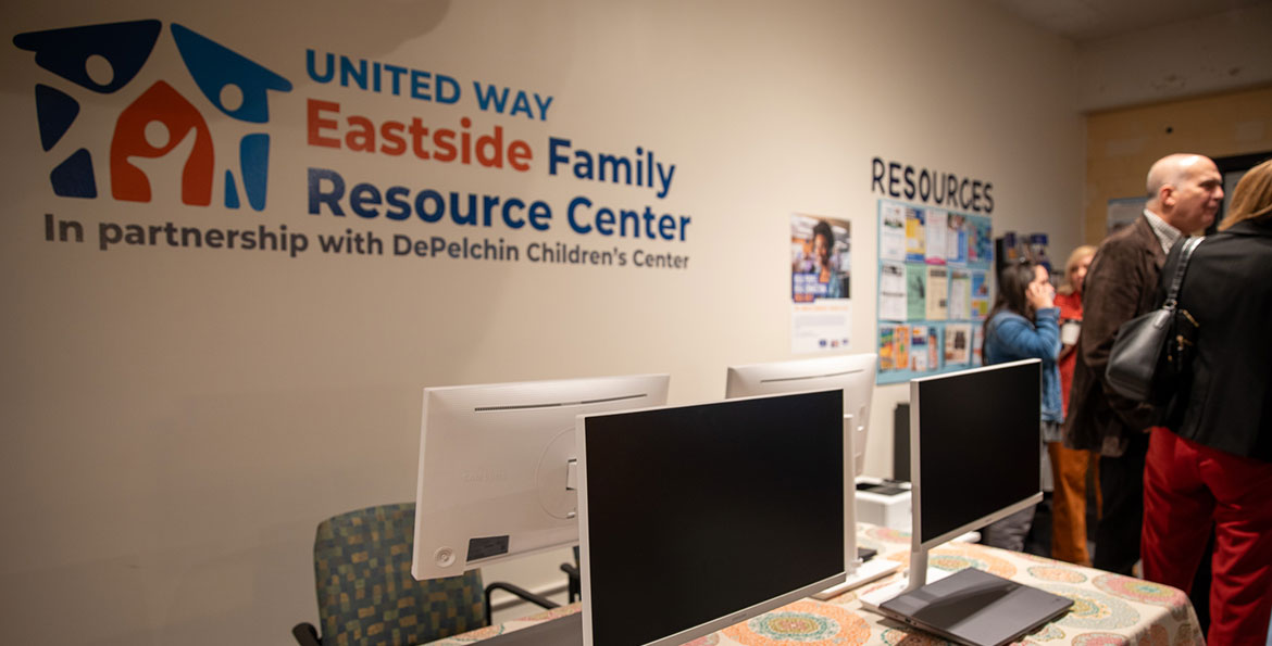 people stand next to a table with computers set up for use inside the United Way Eastside Family Resource Center