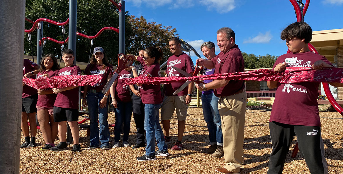 people cutting a large ribbon to commemorate the new Uvalde playspace opening
