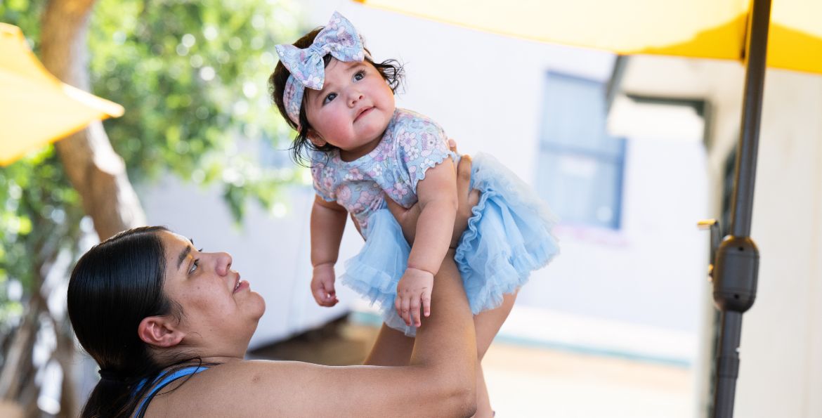 a woman lifts a baby girl into the air playfully